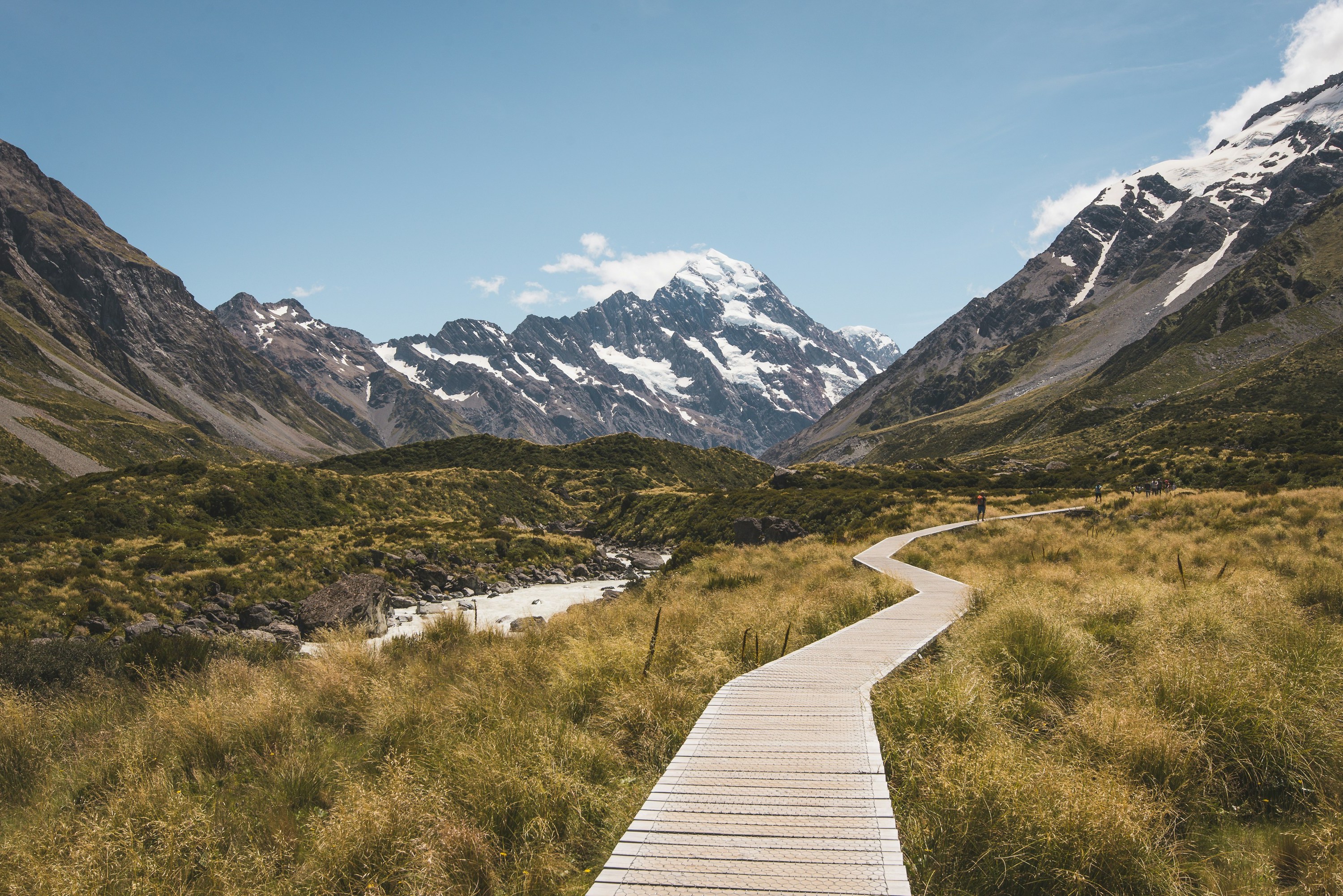 Hikers walking into the distance on a boardwalk through a picturesque New Zealand alpine scene.